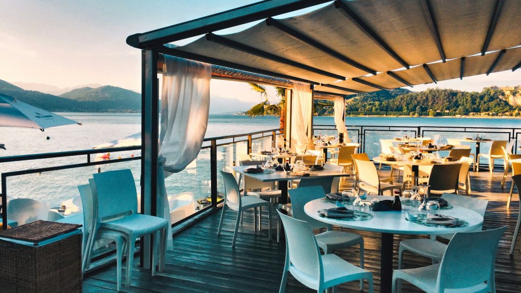 A seafront restaurant terrace laid for dinner at golden hour